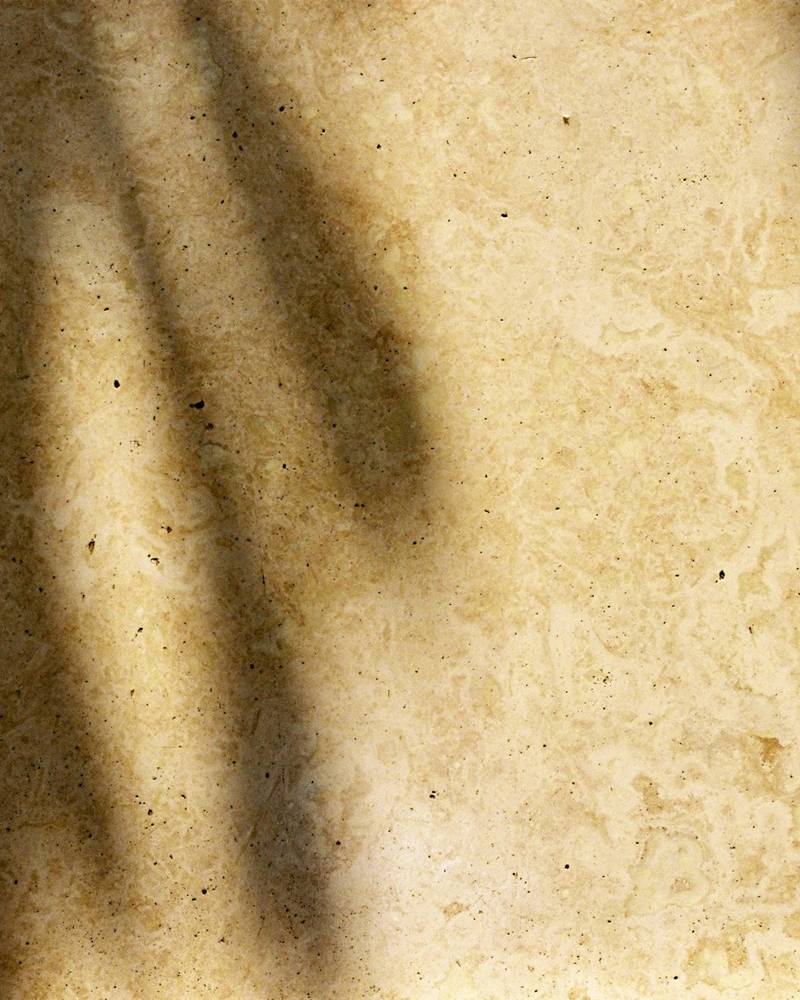 Warm sand-coloured travertine surface crossed by long afternoon shadows