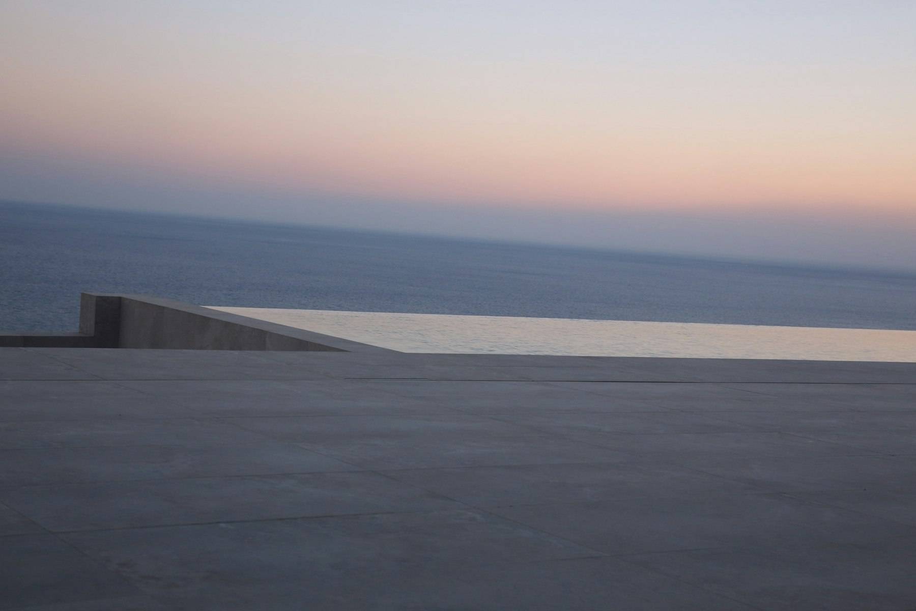 A dark stone plane meeting the sea at dusk, with a thin pale ledge on the horizon
