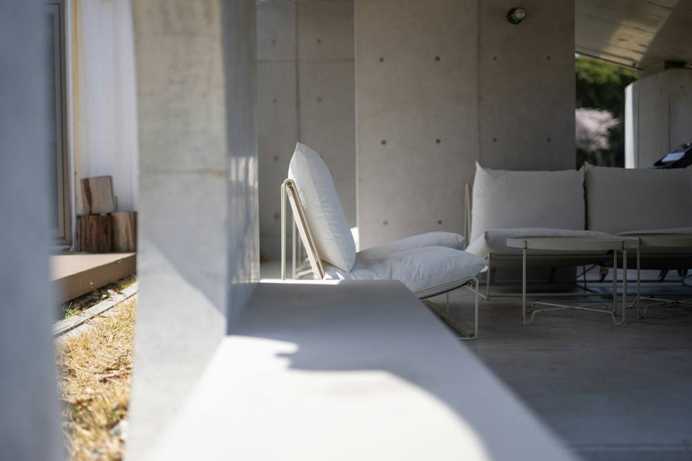 A concrete loggia with low white sofas and a smooth grey floor in soft daylight