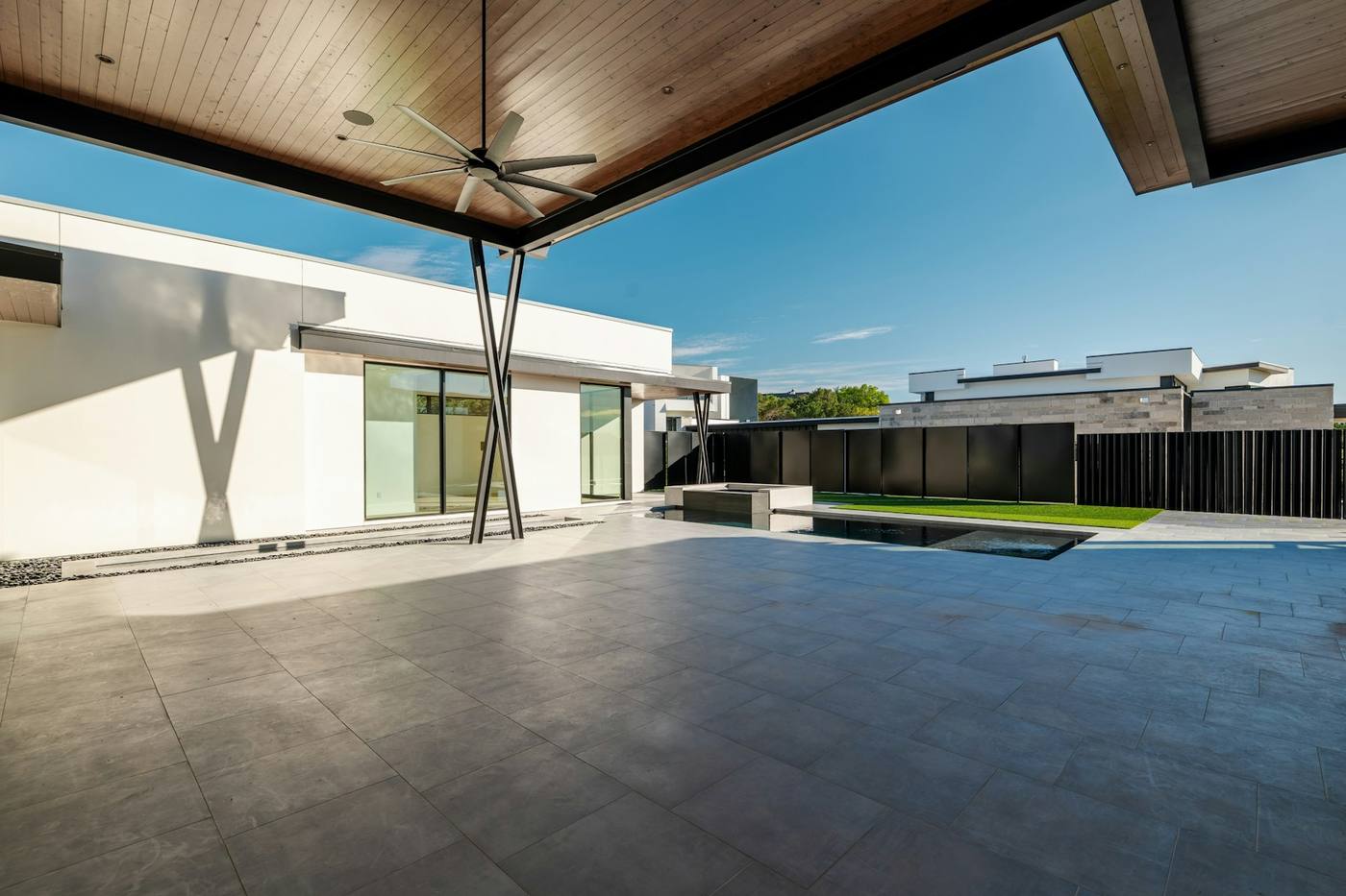 A covered terrace of large grey porcelain slabs leading to a pool beside a white single-storey house