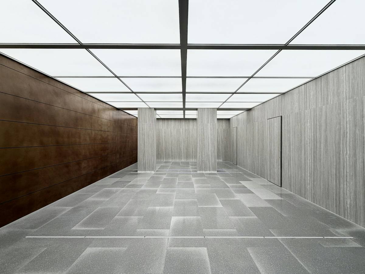 A long top-lit gallery with a grey stone floor laid in large rectangles between timber-clad walls