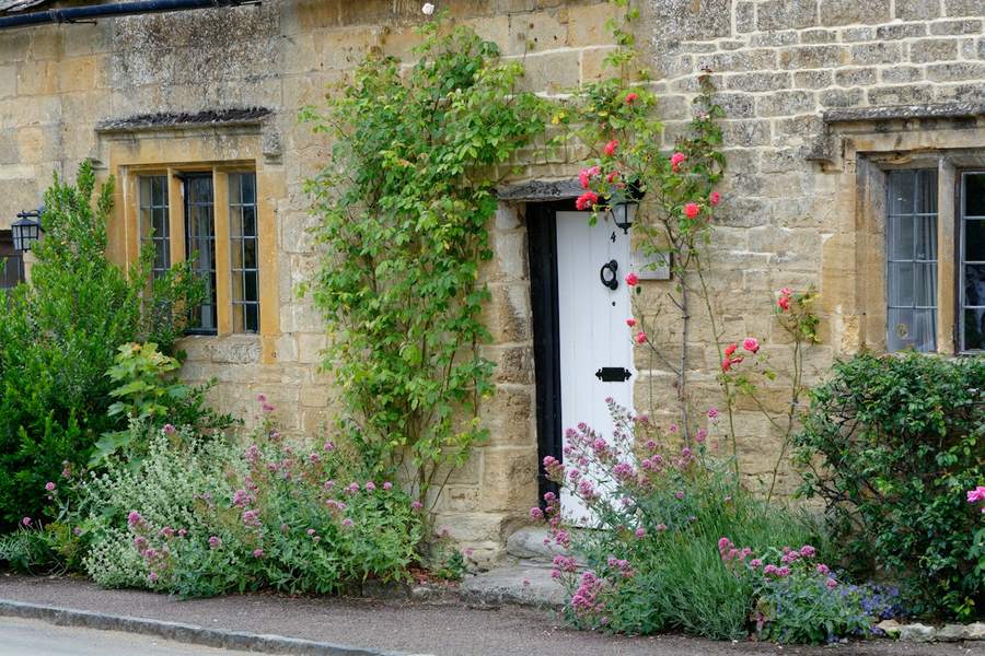 Honey-coloured stone cottage with roses around the door and a stone path