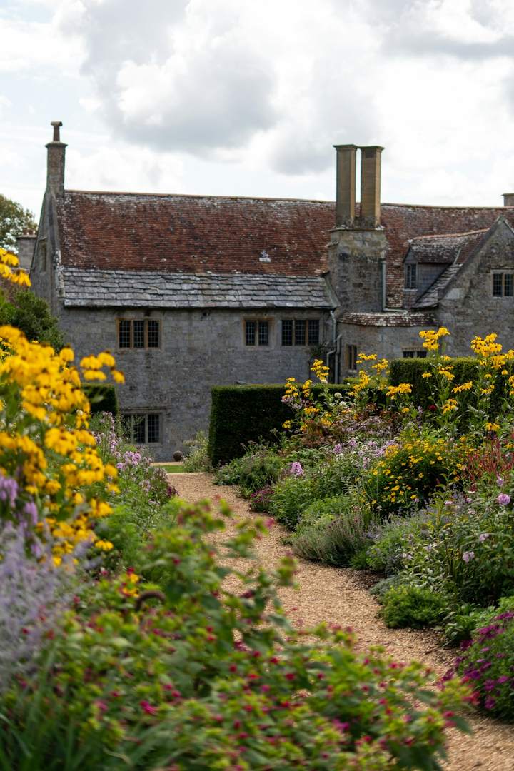 Stone manor house seen along a gravel path between flowering borders