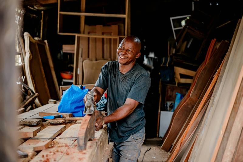 A smiling joiner planes a length of timber in his workshop