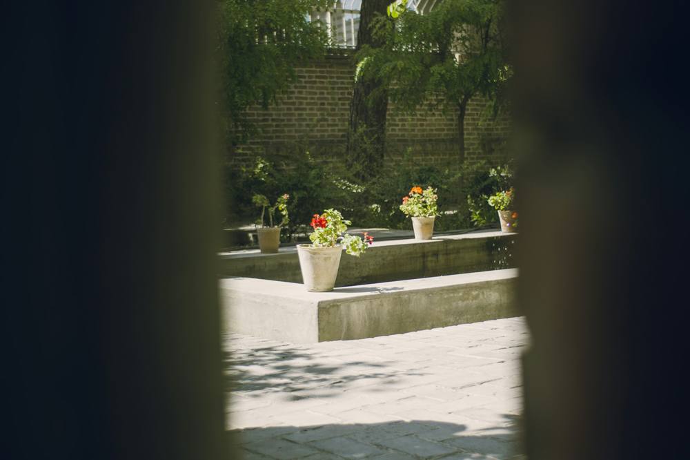 A sunlit courtyard seen through a dark doorway, with stone planters and potted geraniums