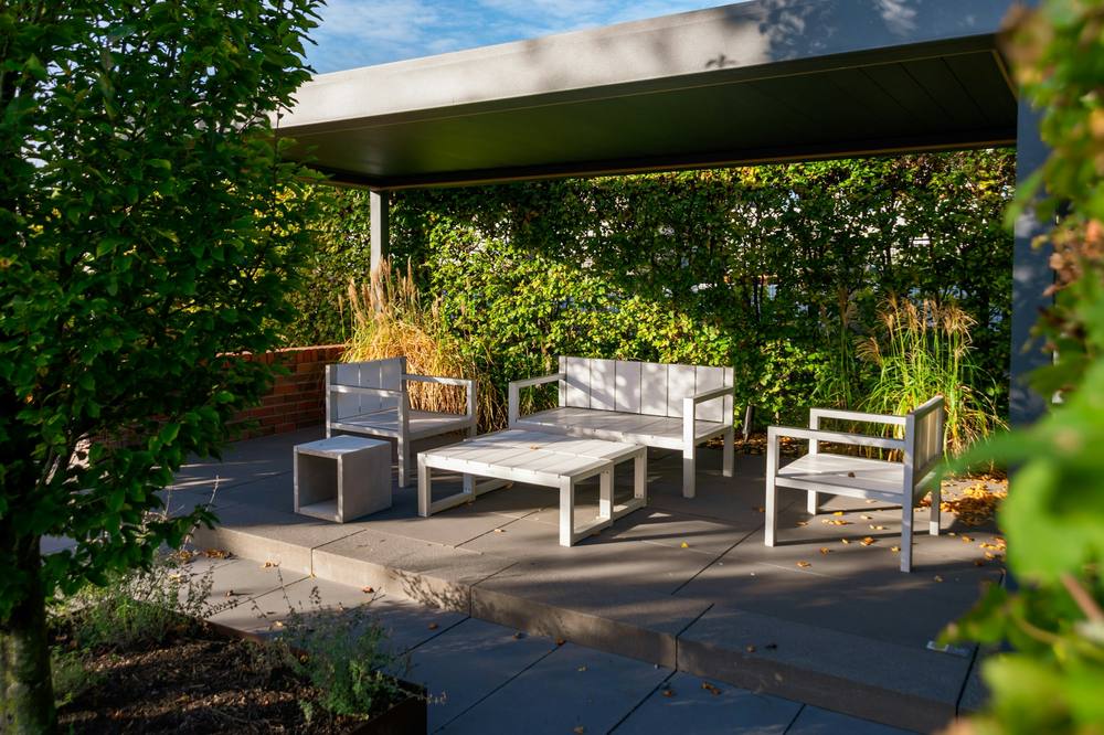 Covered roof terrace with dark paving, pale outdoor furniture and tall grasses in evening light