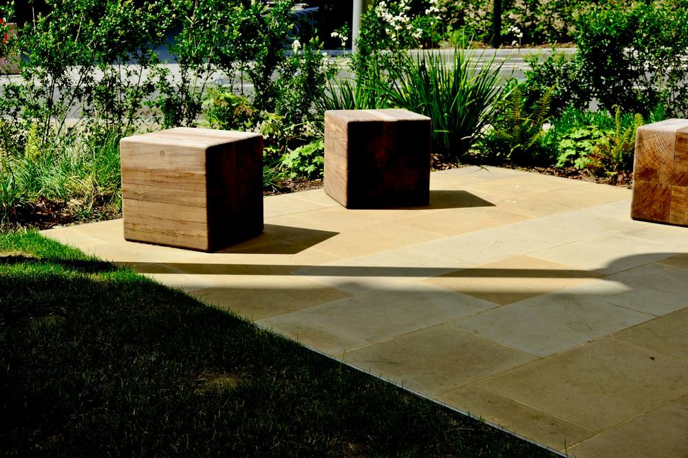 Warm sandstone terrace in sunlight with three timber block seats and lush planting