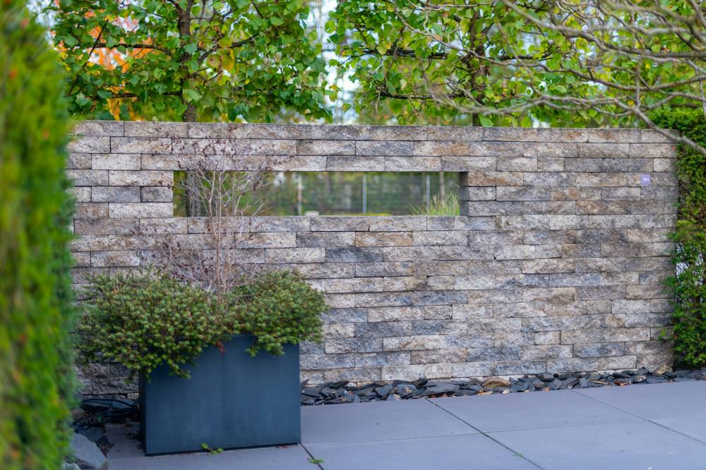 Grey porcelain paving in front of a split-face stone screen wall with a slot window and a planter